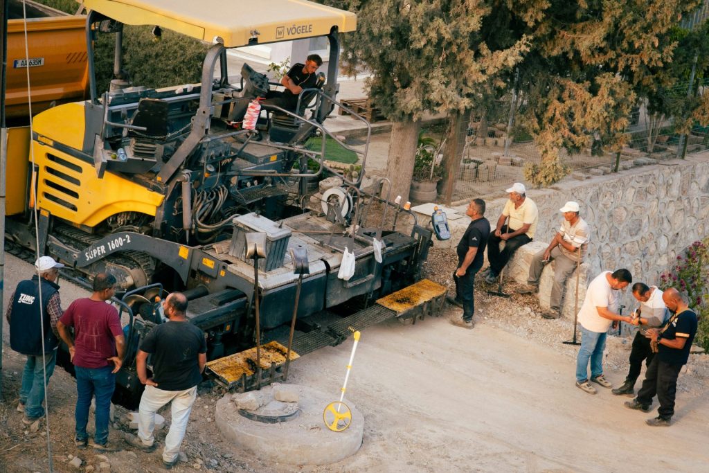 Construction workers operate asphalt paving machinery on road.